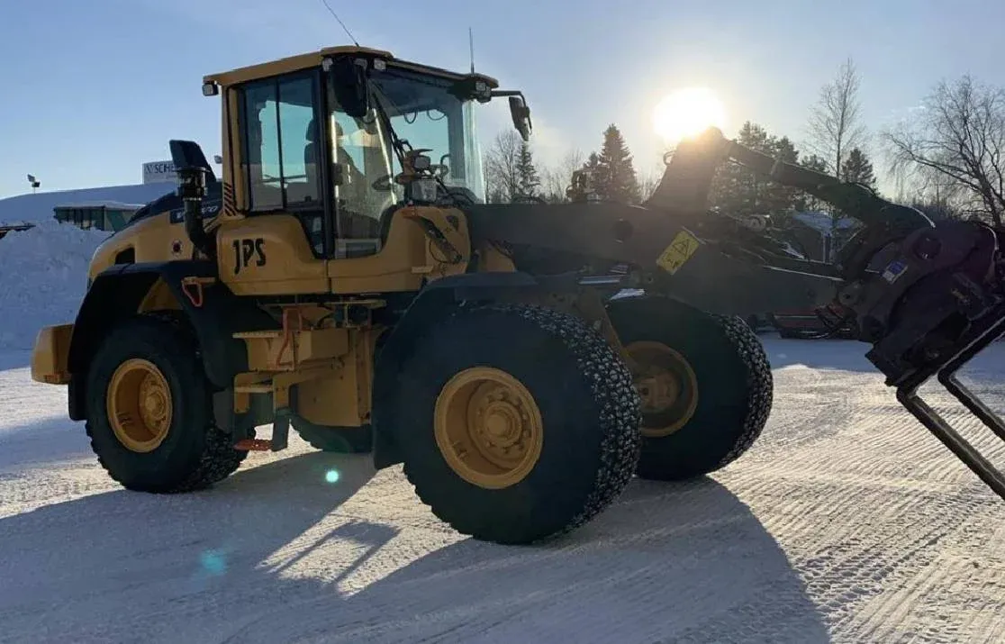 Hjullastare med JPS-märkning och tända arbetsljus på snötäckt gårdsplan.