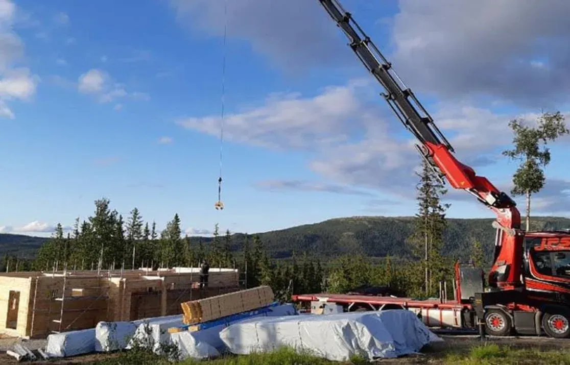 Kranbil som lyfter byggmaterial vid en byggplats i skogen.