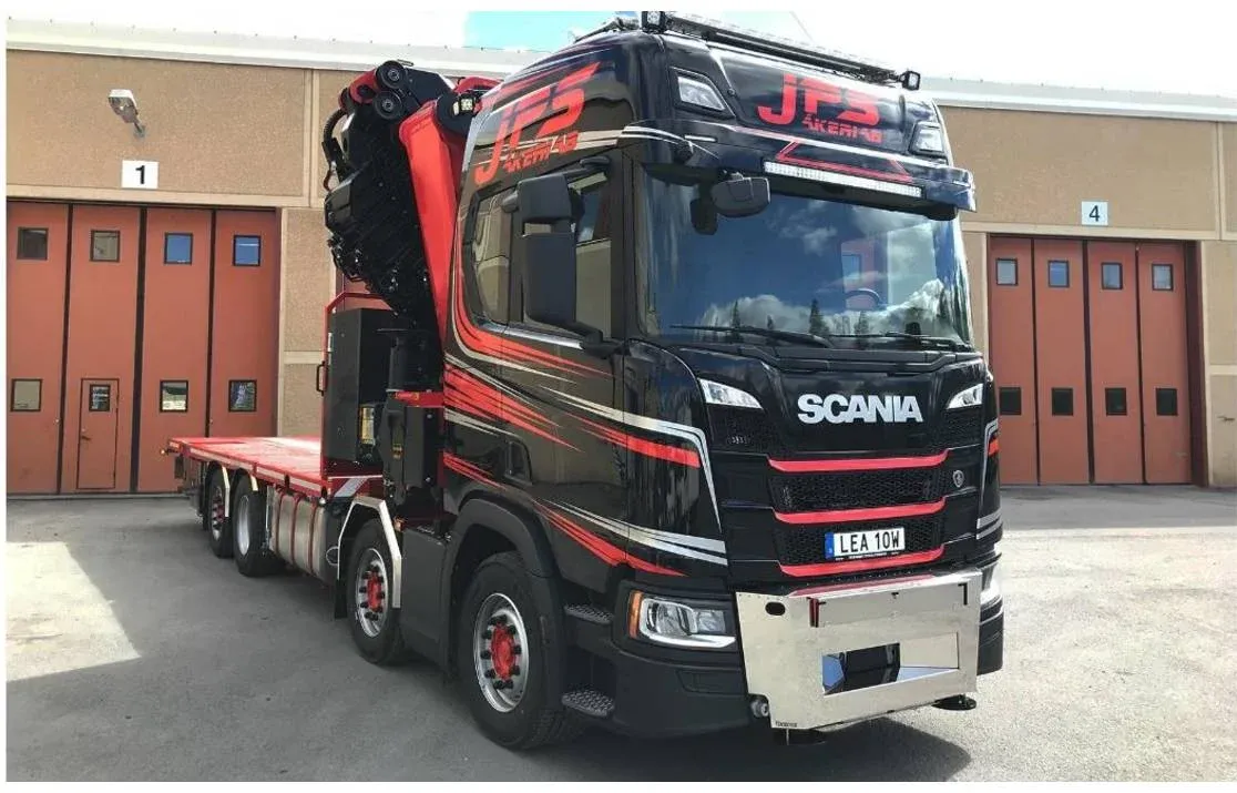 Svart Scania kranbil med röd kran uppställd framför garageportar.