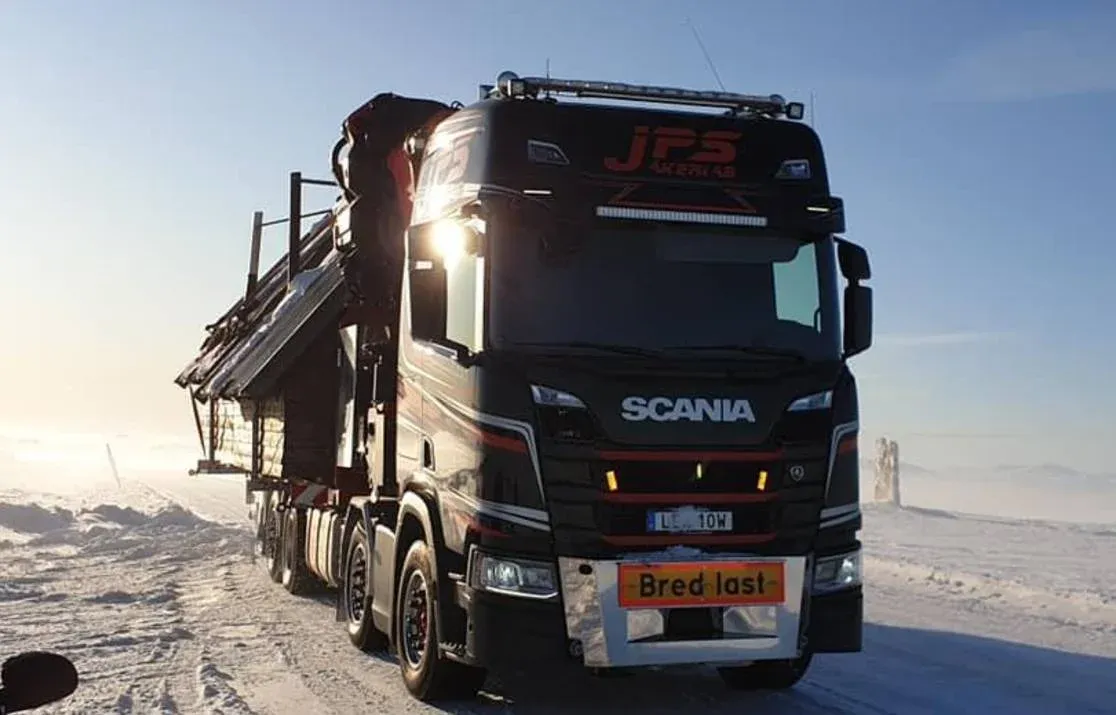 Scania kranbil i motljus på snötäckt mark med tända strålkastare.