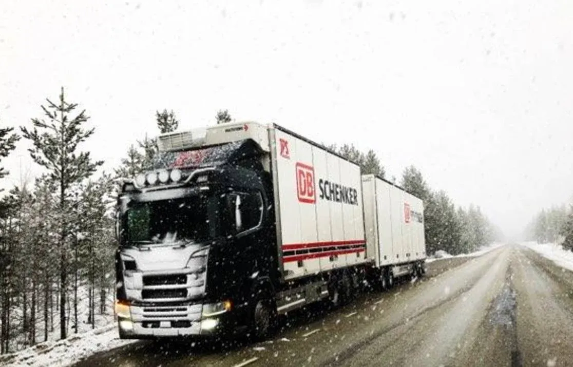 Scania med DB Schenker-ekipage kör genom snöyra på en skogsväg.