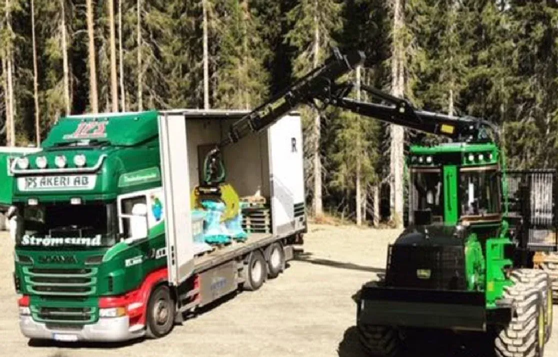 Scania från Strömsund lastar gods bredvid en skogsmaskin i skogen.